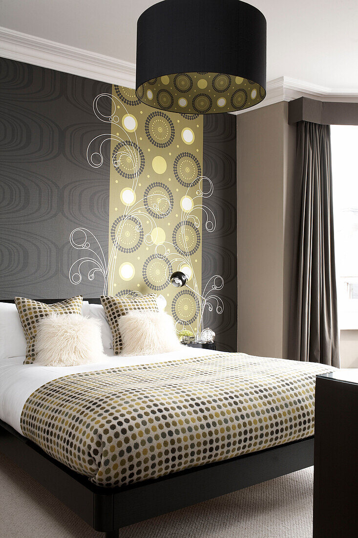 Doppelbett mit gepunkteter Bettdecke und dazu passender Tapete und Lampenschirm