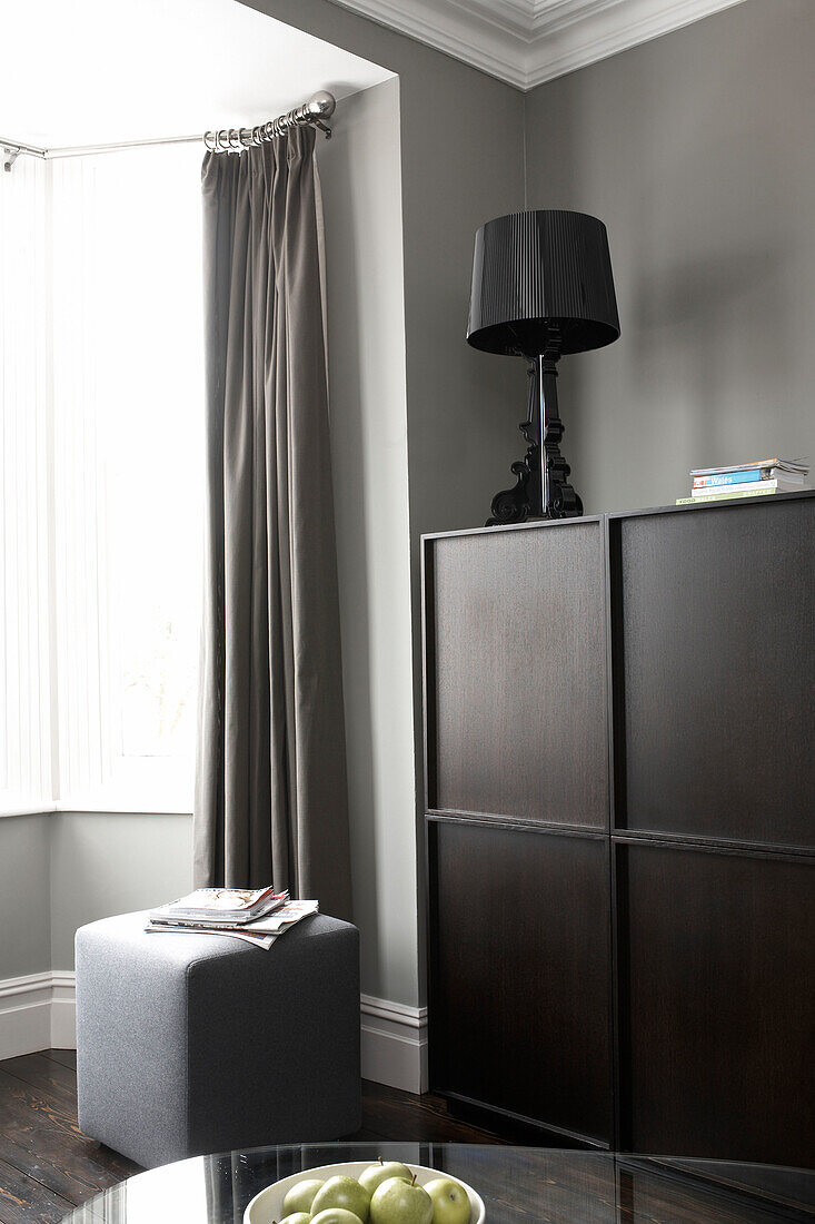 Dark wood storage unit with lamp at bay window of grey living room