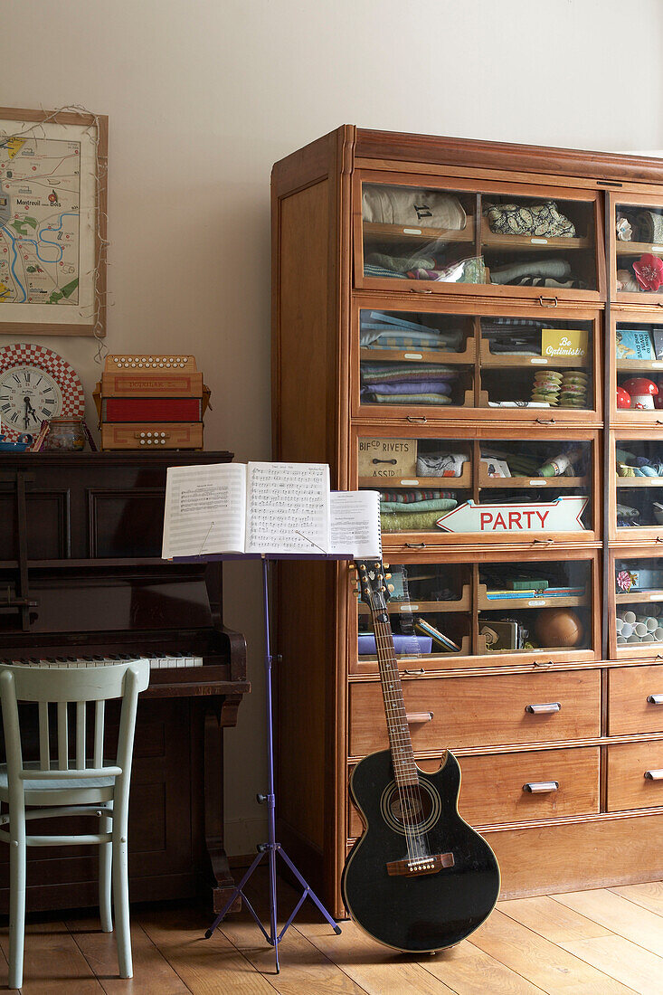 Guitar and music stand with piano and glass fronted cabinet