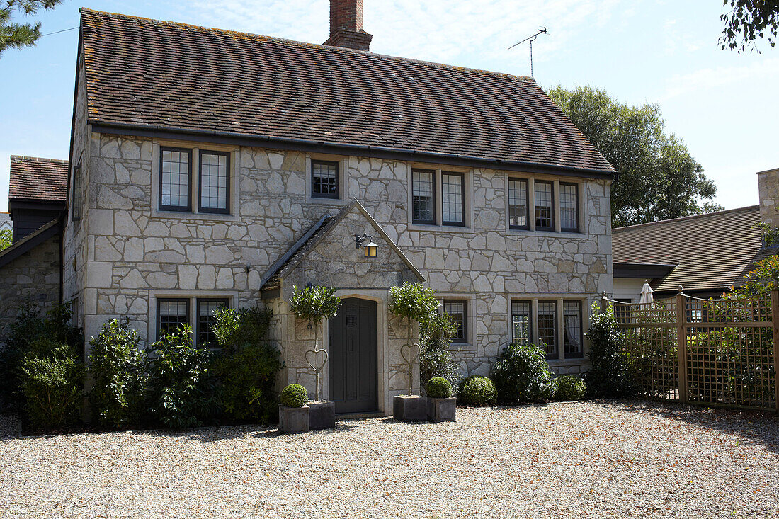 Steinfassade eines freistehenden Hauses mit Kiesauffahrt und Topfpflanzen in Brook, Isle of Wight, Vereinigtes Königreich