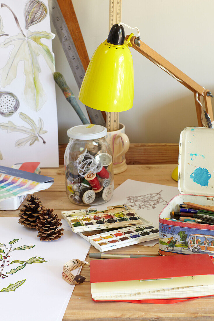 Yellow lamp and jar of threads with art equipment in Wiltshire home, England, UK