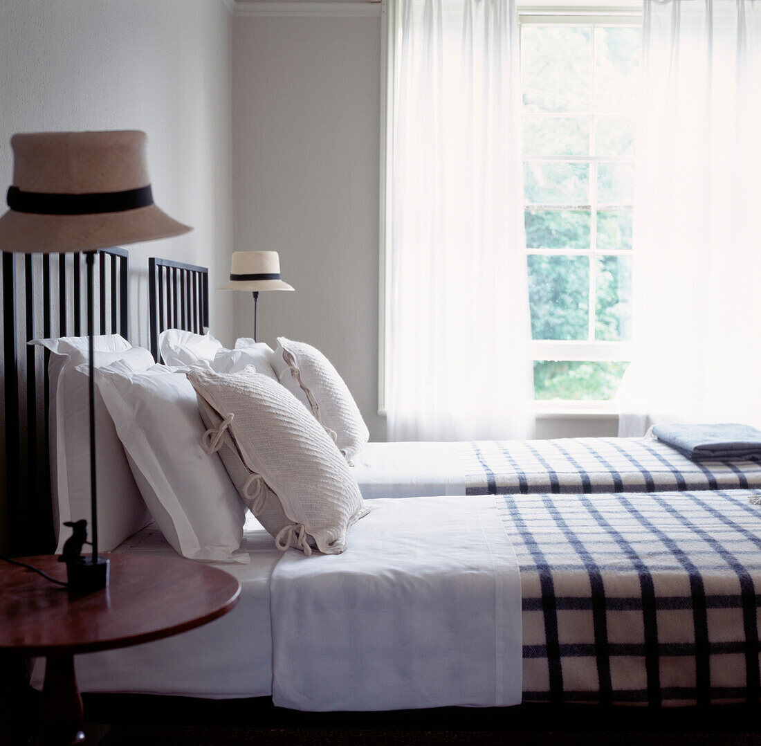 Twin beds in guest bedroom with straw hat bedside lamps and open window