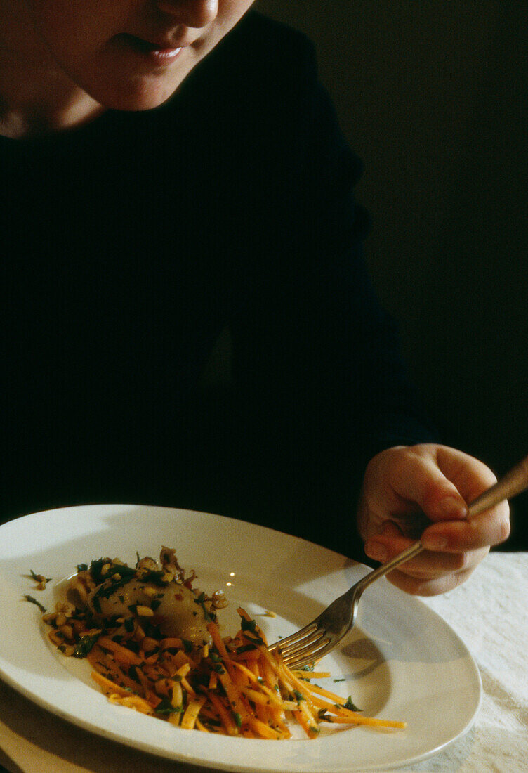 Frau isst mit Gabel Tintenfisch und Karottensalat