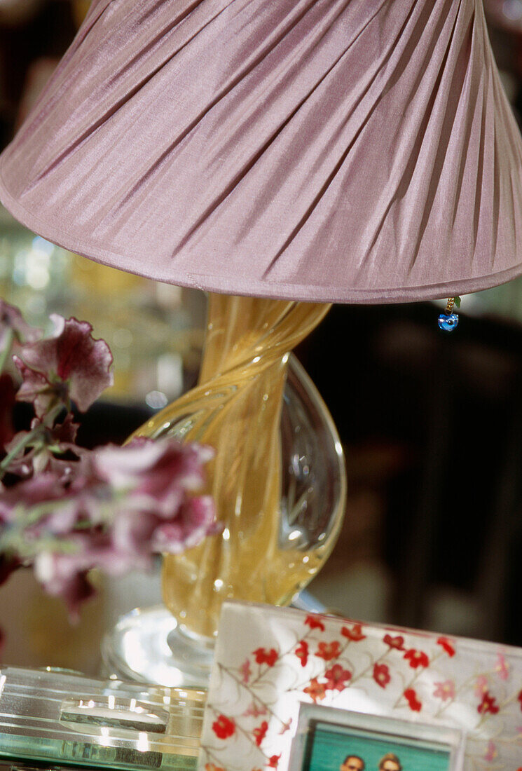 Detail of twisted glass table lamp stand with pink silk lampshade with flowers and photo in foreground