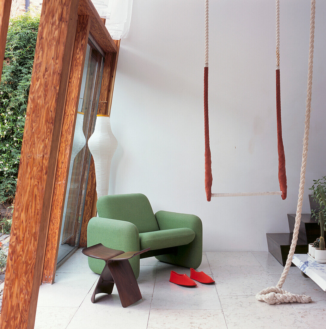 A green 60's armchair with indoor trapeze next to the sloping glass picture window of modern terrace conversion