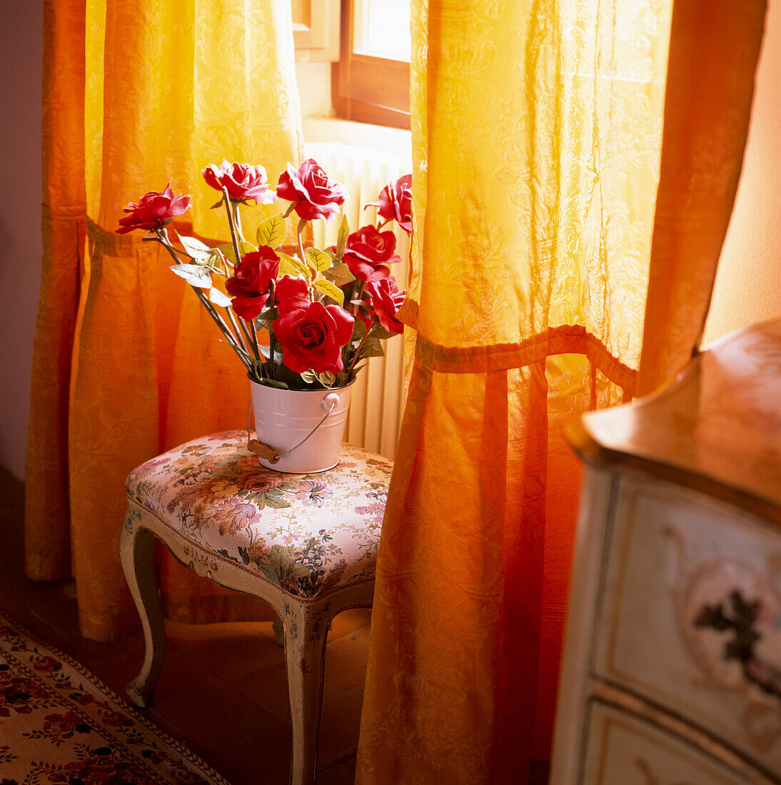 Detail of window with red roses on a baroque stool and gold curtains