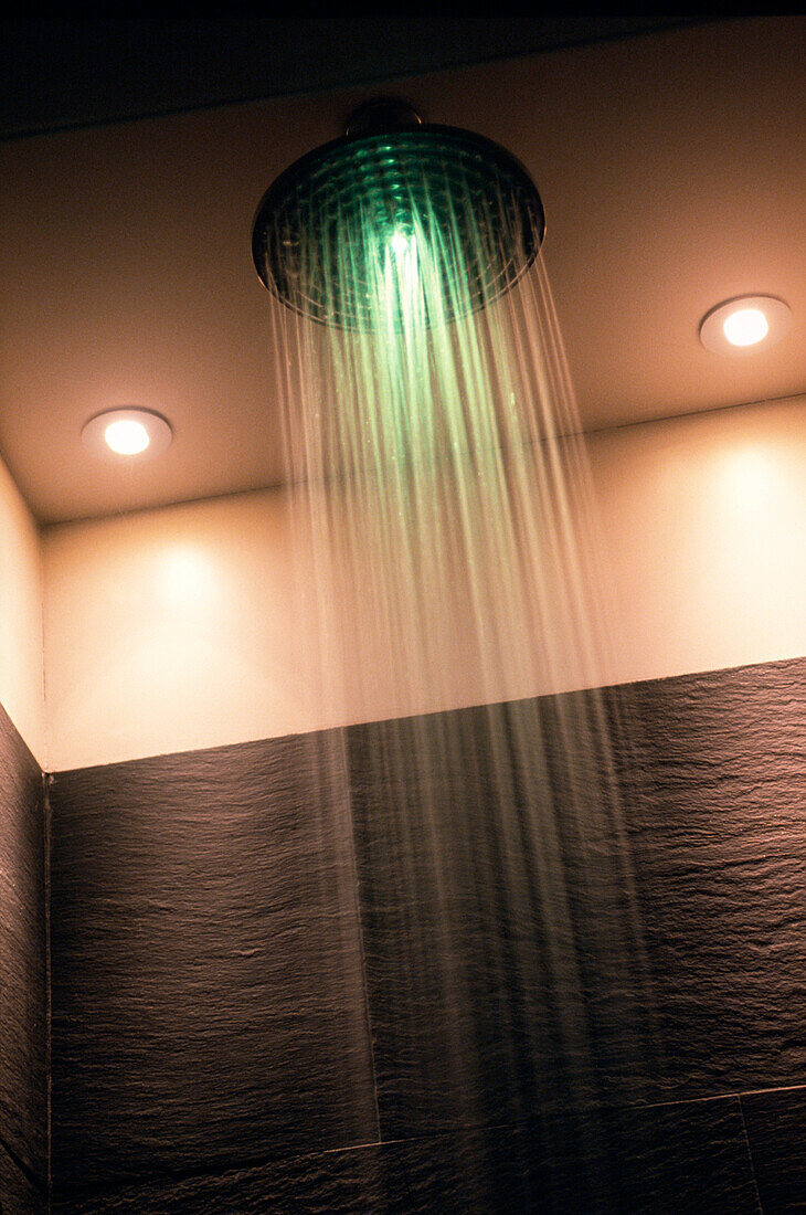 Duschkopf in einem mit Schiefer gefliesten Badezimmer mit grünem Licht, das sich im Wasser spiegelt