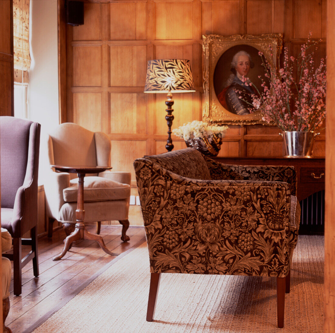 Floral print sofa and armchair in wood panelled lounge with large bouquet and wooden lamps illuminating the room