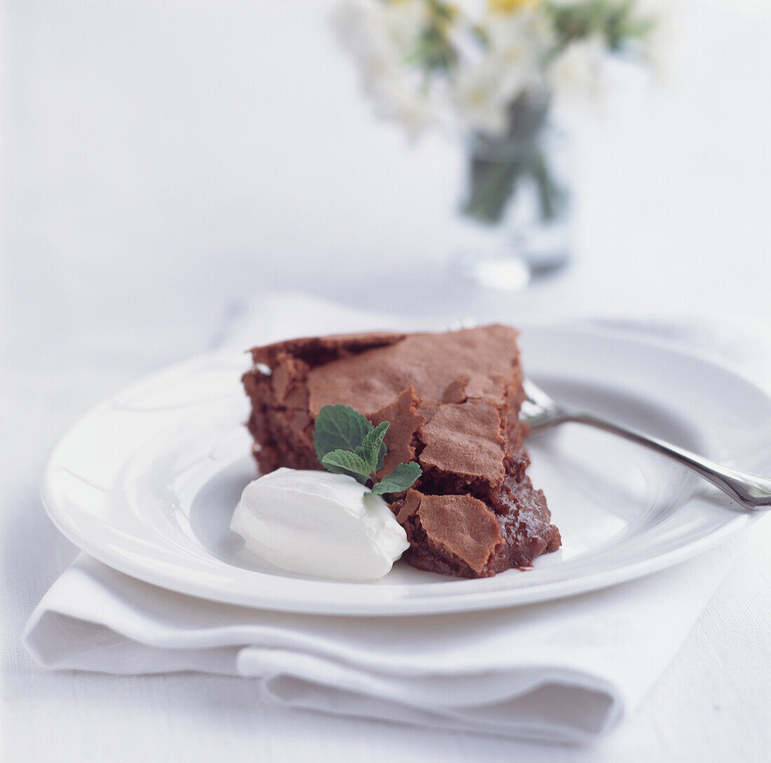 Schokoladenkuchen mit Mandeln und Armagnac, serviert mit Sahne und Minze auf einem weißen Teller
