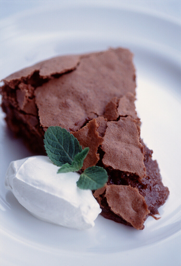 Chocolate almond and Armagnac cake served with cream and mint served on a white plate