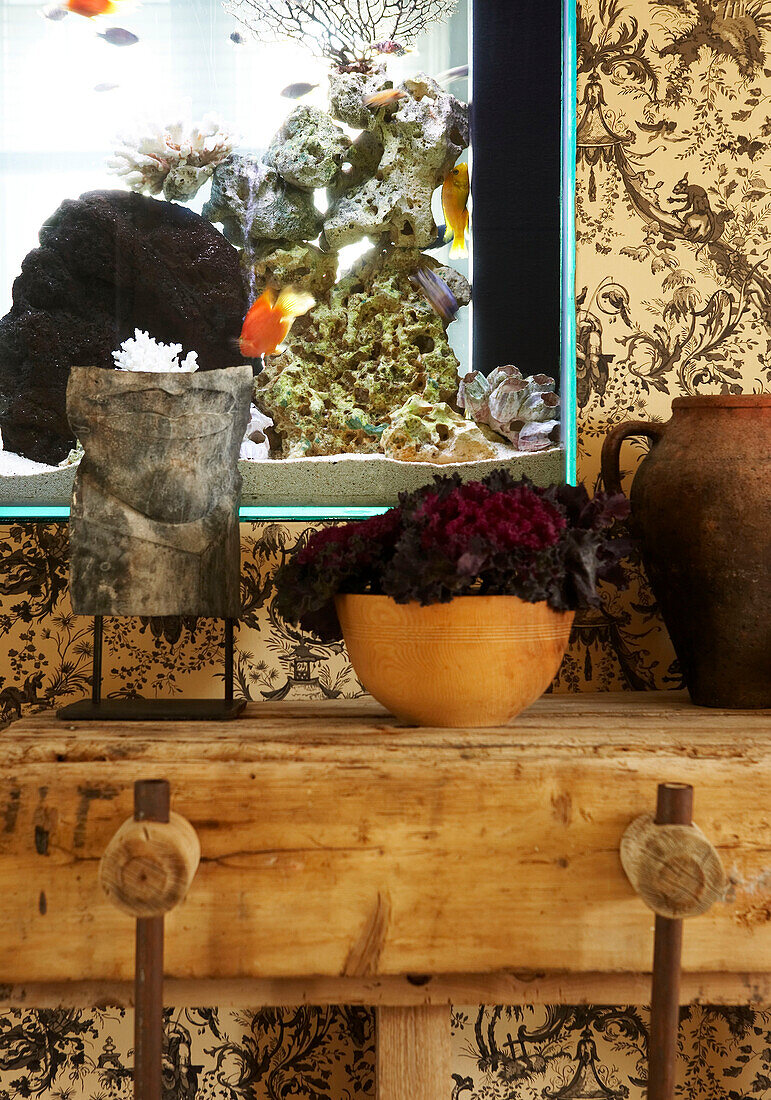 Detail of built in aquarium with fish swimming behind a collection of vintage pottery on an old workbench