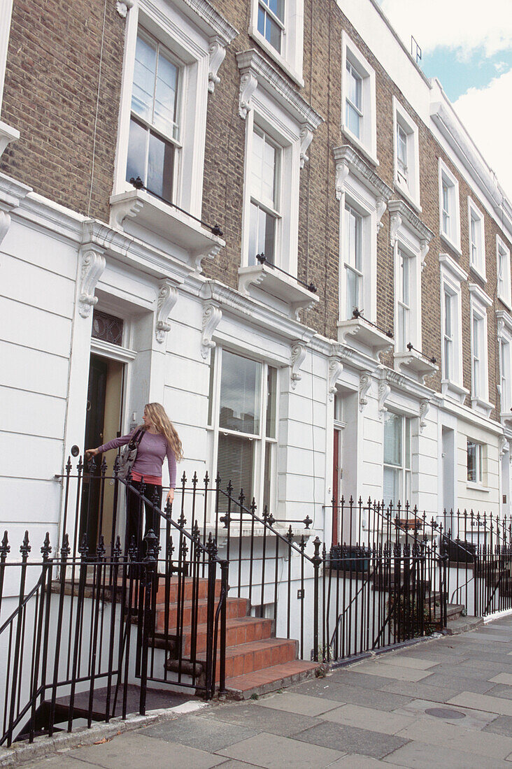 Außenansicht einer Reihe viktorianischer Londoner Stadthäuser mit einer jungen Frau, die die Tür schließt