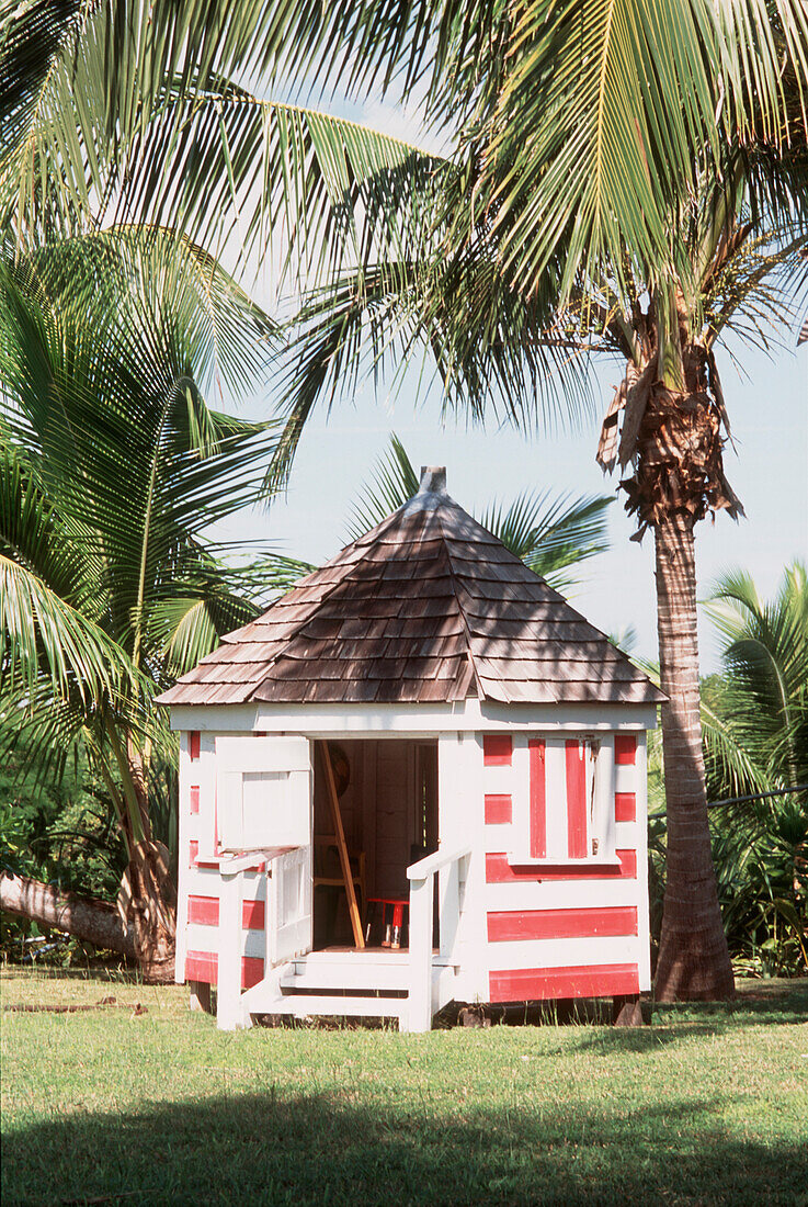 Red and white striped painted playhouse in a tropical garden