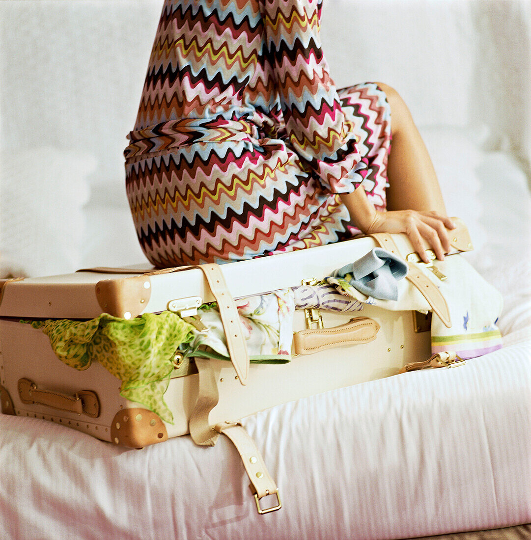 Junge Frau sitzt auf einem überfüllten Koffer auf einem Bett