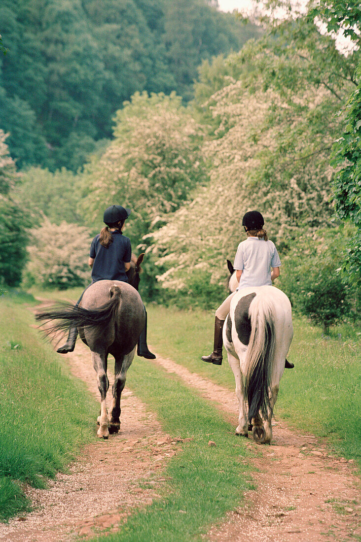 Two girls riding horses on country lane