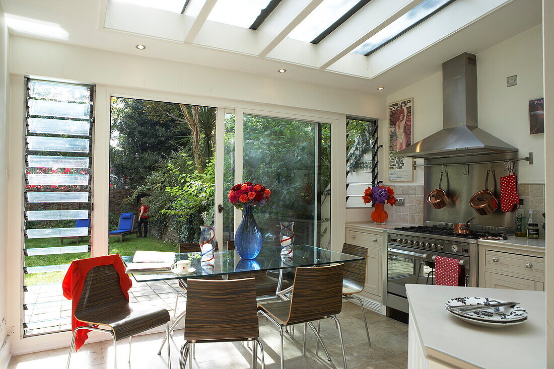 Glass table in London kitchen extension with view through sliding doors to garden, England, UK