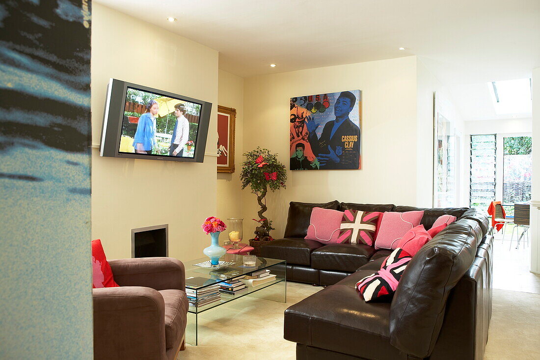 Brown leather seating with wall mounted television in living room of funky London home, England, UK