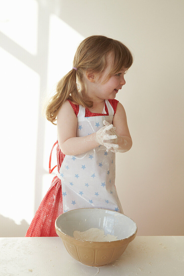 Young girl in red dress stands mixing flour in a bowl
