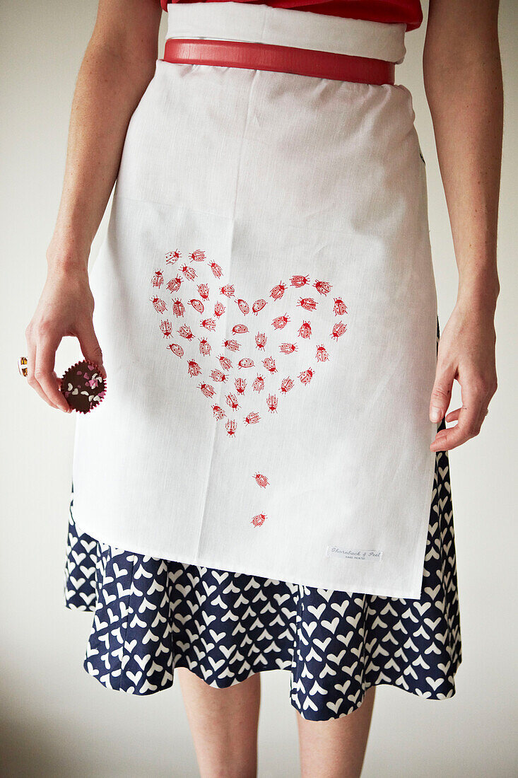 Frau in herzförmiger Schürze mit roten Muffins in der Hand (Unterer Ausschnitt)