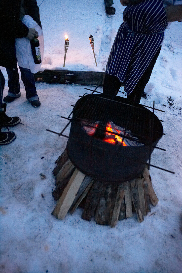People stand near barbecue grill with burning embers in snow, Zermatt, Valais, Switzerland