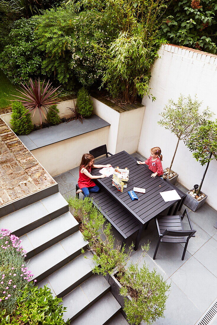 Erhöhte Ansicht von zwei Mädchen, die im Innenhof einer Terrasse an einem Tisch sitzen, London, England, UK