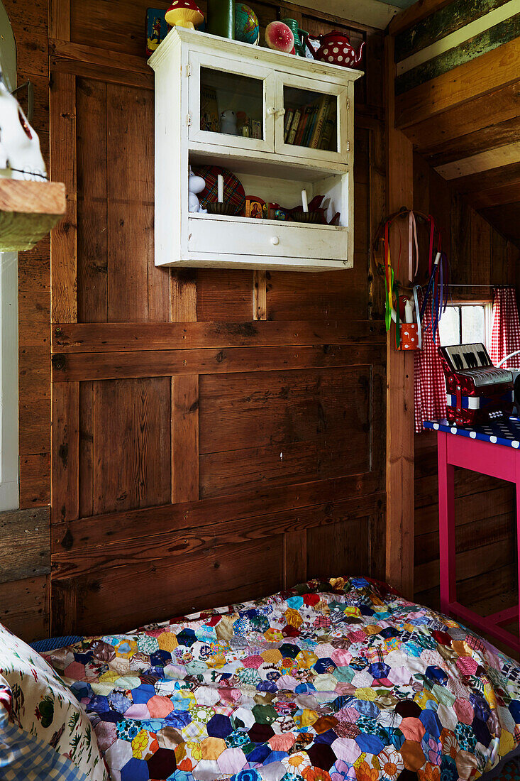 Wall-mounted cabinet above single bed with patchwork in wood-panelled Rye treehouse, East Sussex, England, UK