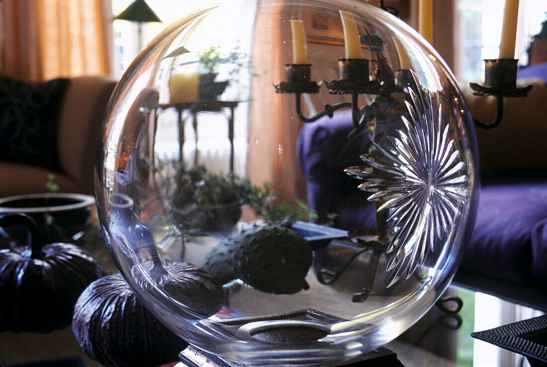 Blick durch geschliffene Glaskugel auf getrocknete Kürbisse und Kerzenständer aus Metall