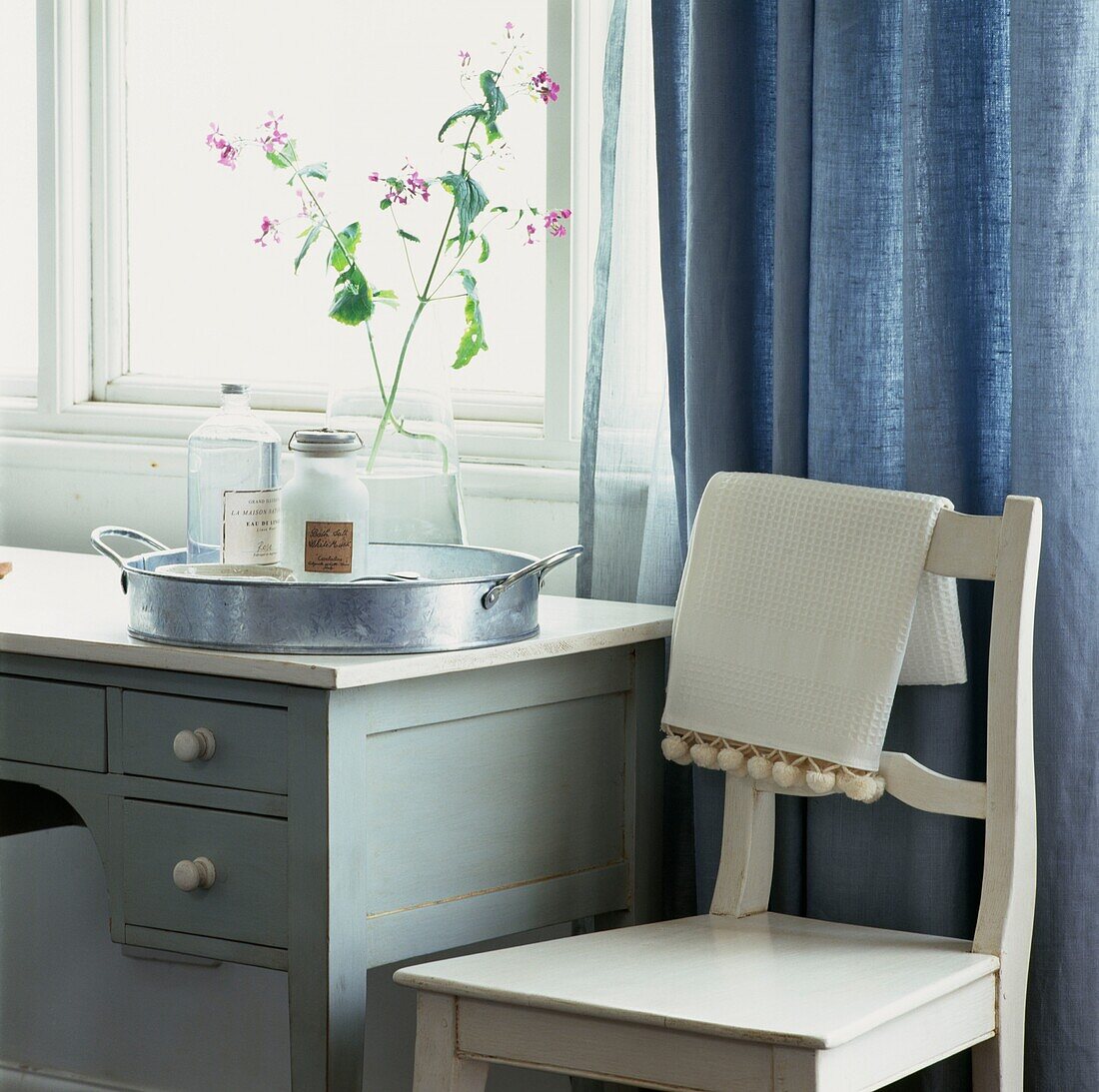 Toiletries and silver tray on dressing table at curtained window with chair