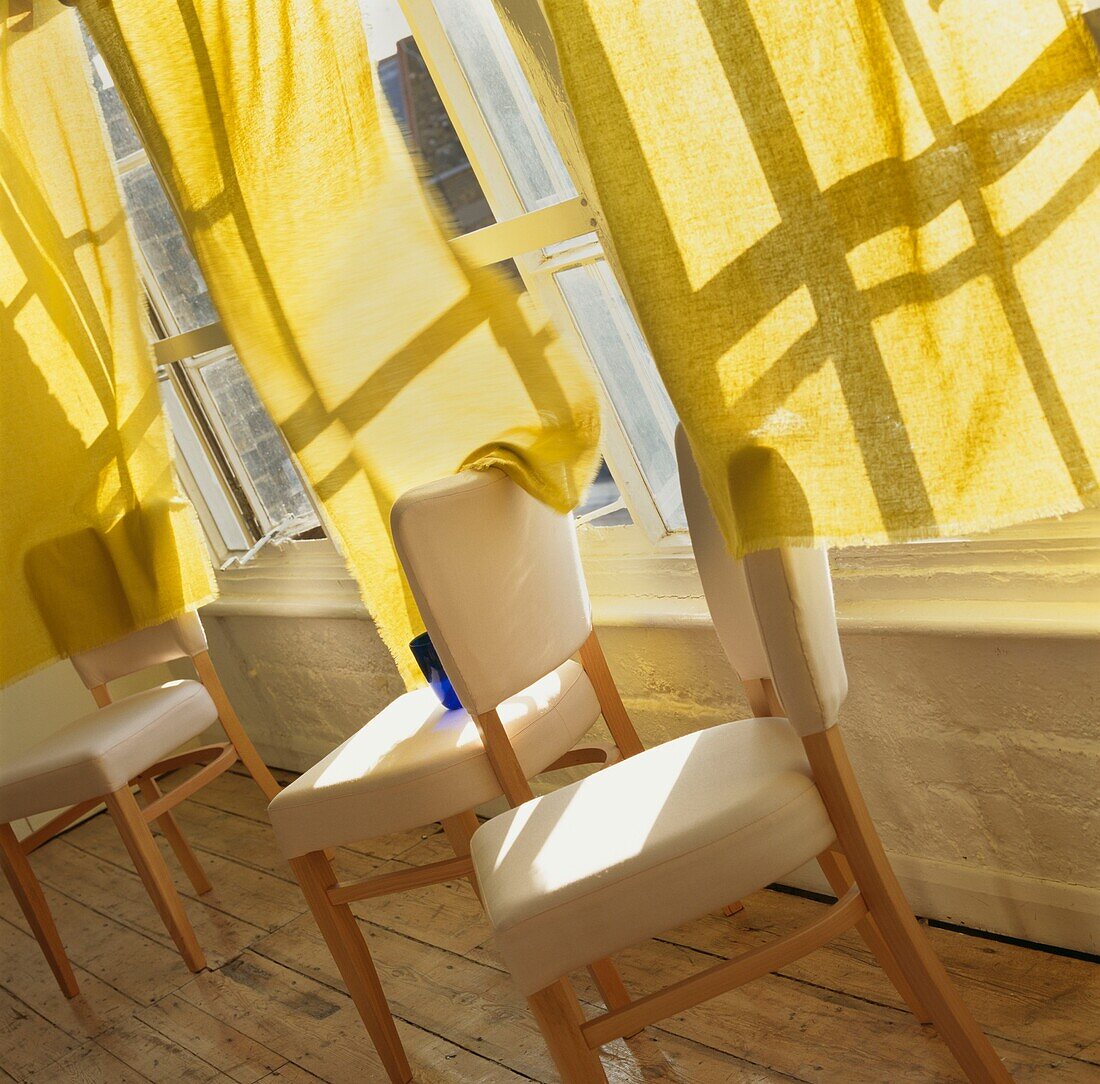 Three cream dining chairs at window with yellow curtains