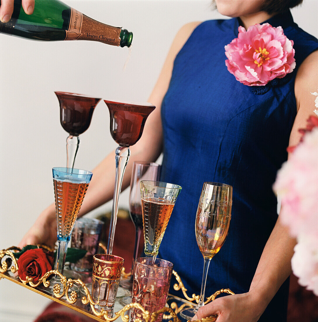 Woman holding an ornate tray of champagne glasses with man pouring from bottle