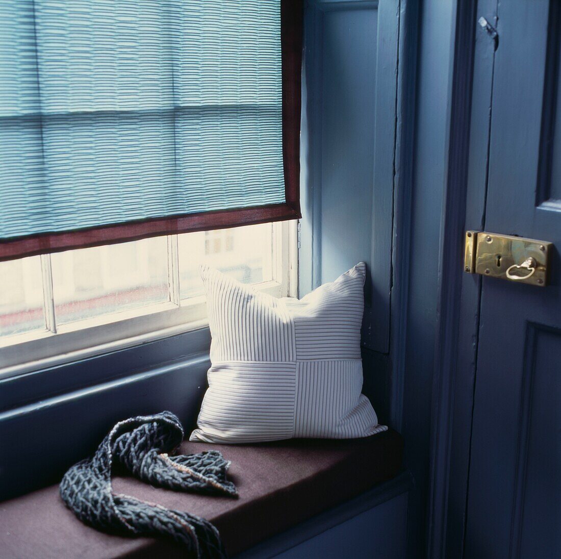 Cushion and scarf on window seat with turquoise blind and brass lock and key