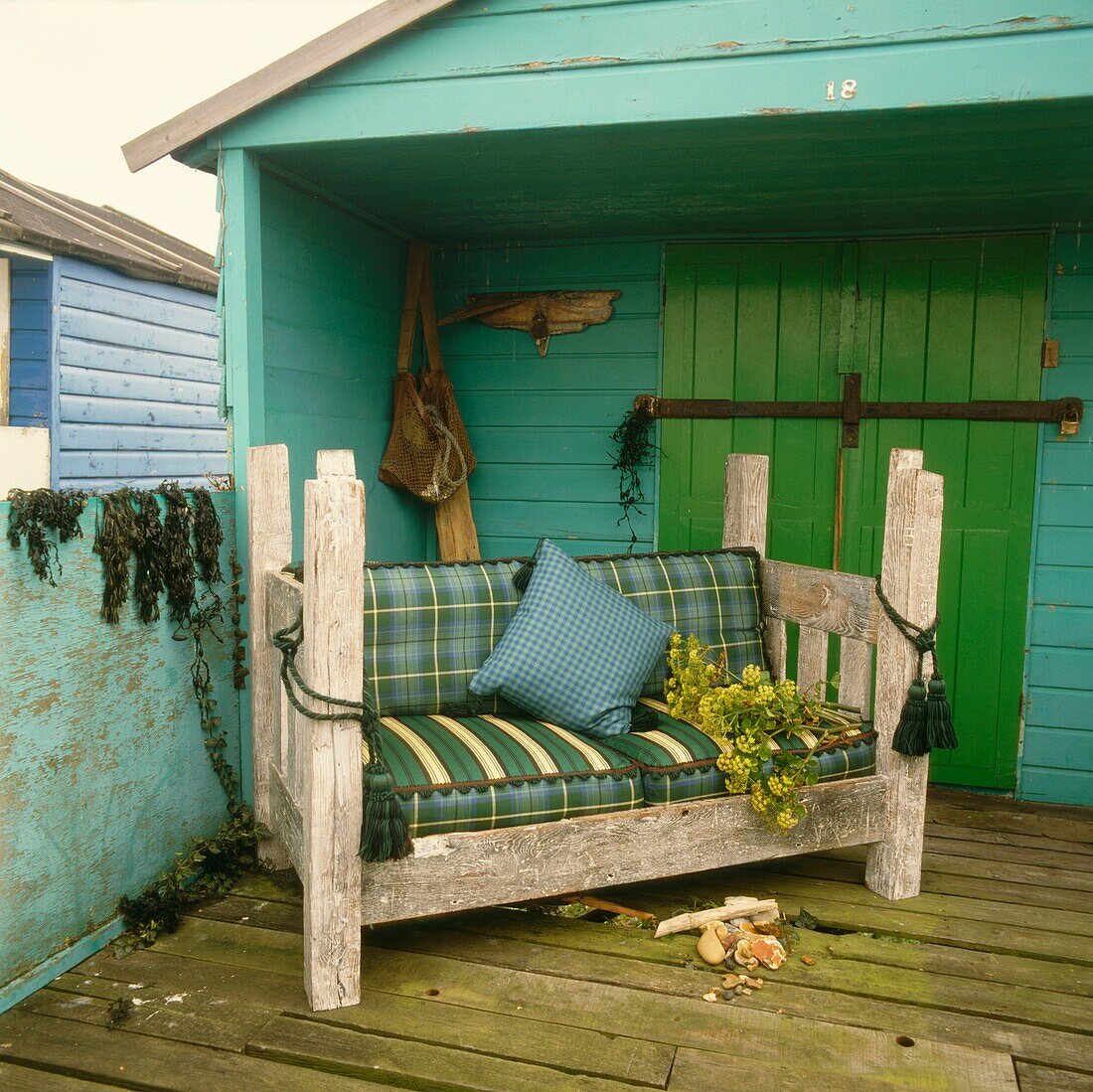 Holzsofa mit karierten Stoffkissen auf der Veranda eines grün gestrichenen Strandhauses