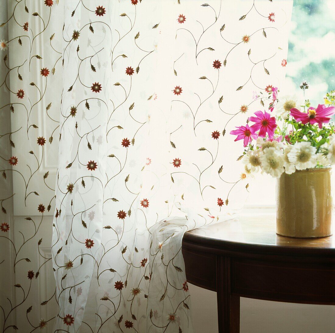 Vase of wildflowers on table at window with floral patterned curtains