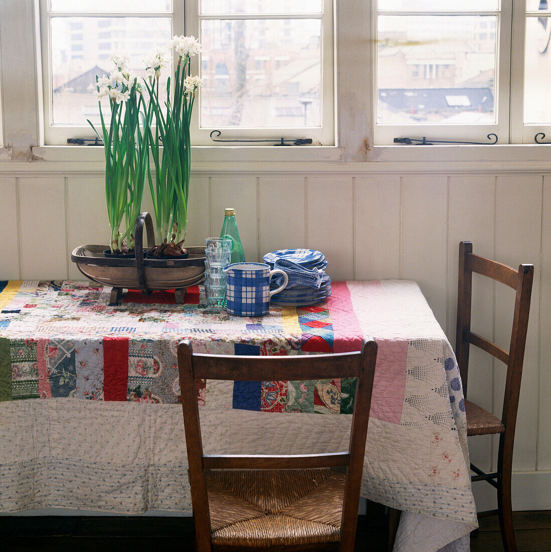 Kitchen table in panelled room with daffodils on a brightly coloured patchwork tablecloth