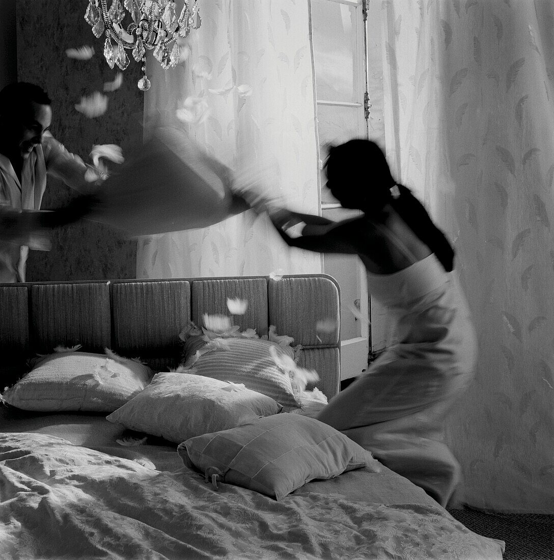 Couple have a pillow fight on a bed in a bedroom