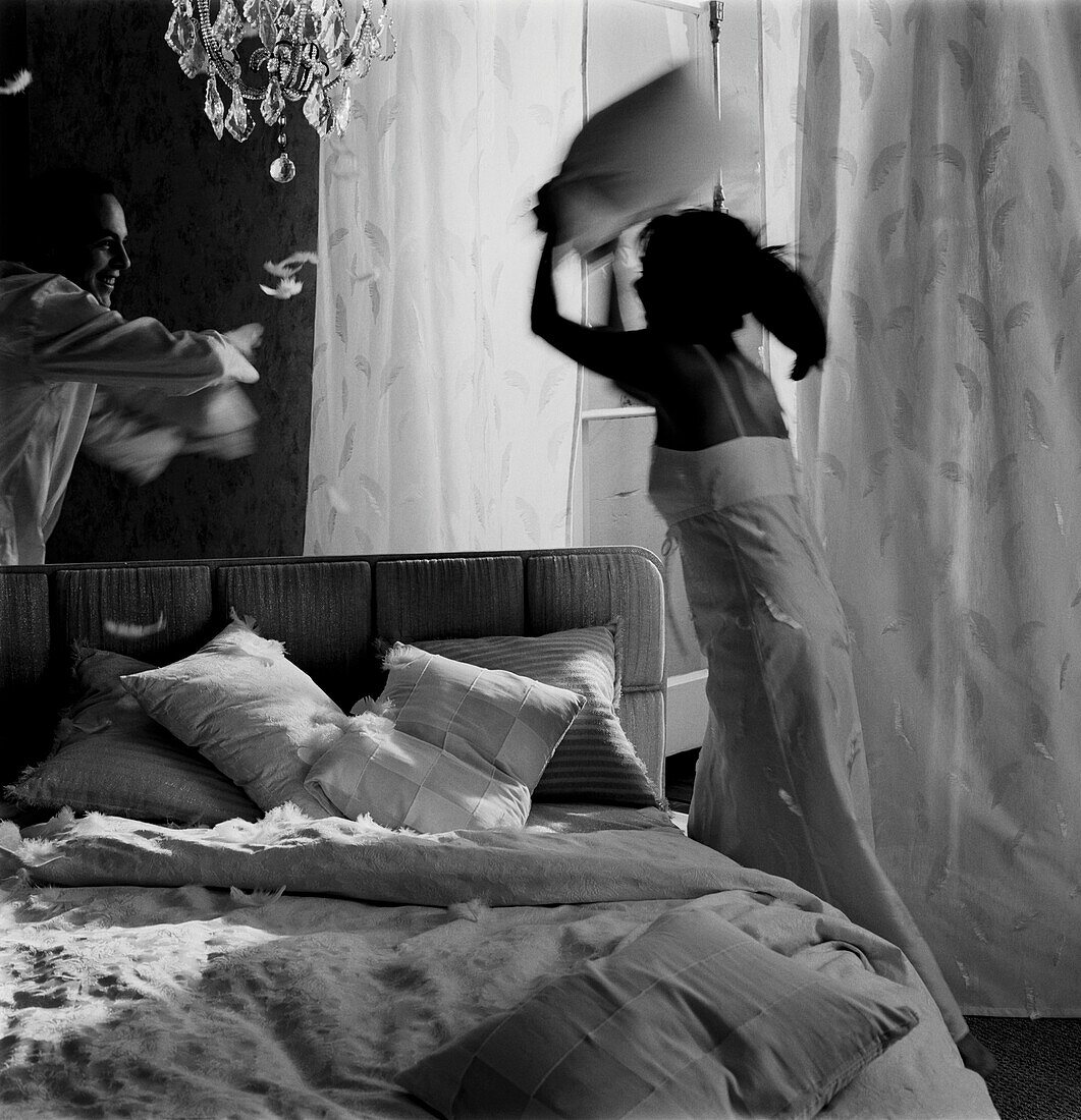 Couple have a pillow fight on a bed in a bedroom
