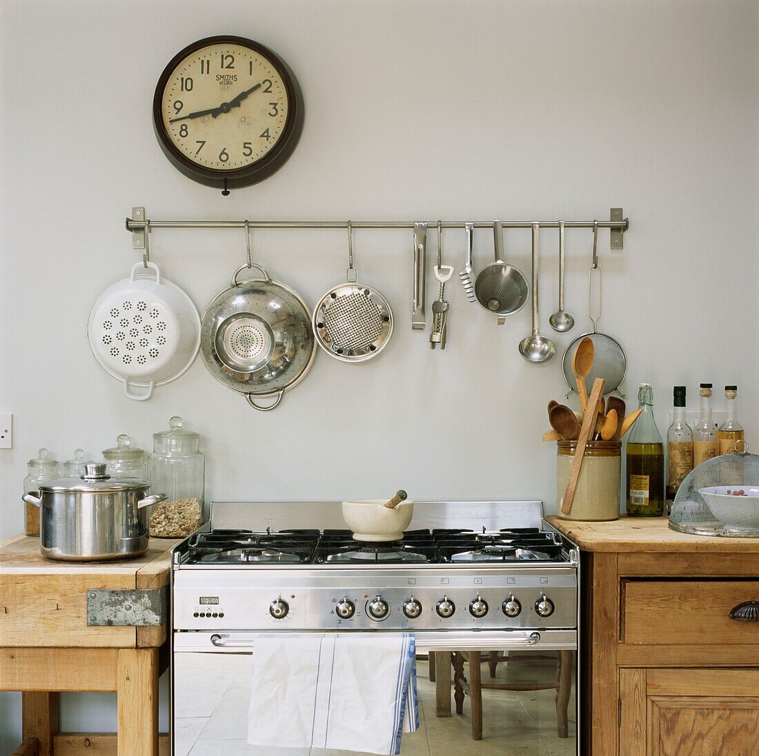 Colanders hang under clock above stainless steel oven