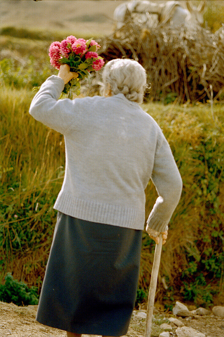 Ältere spanische Dame mit einem Strauß rosa Blumen auf dem Lande in Rioja