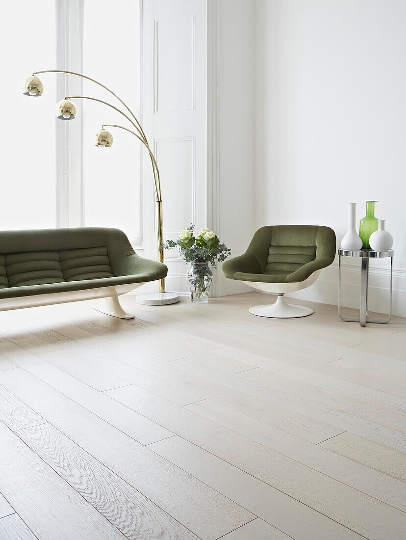 Green retro style armchair and sofa in living room with painted white floorboards