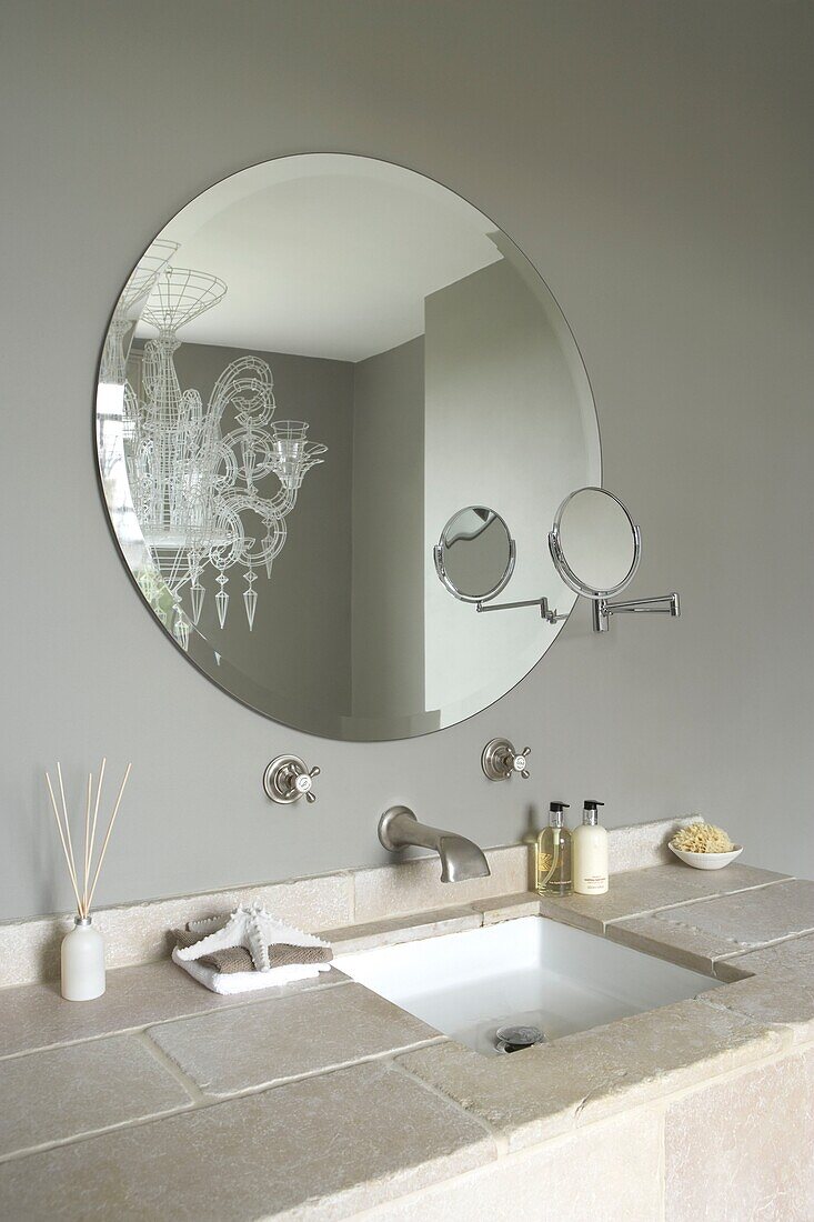 Close up of bathroom sink with tiled counter top and round mirror