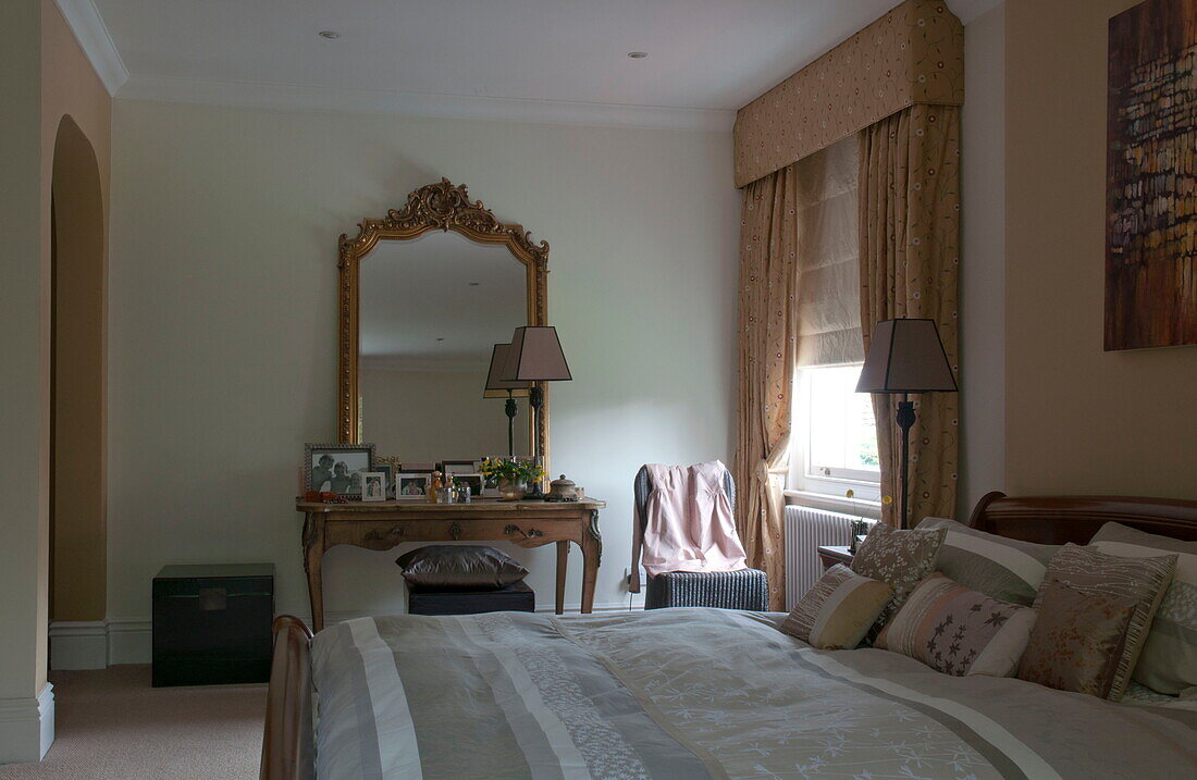 Gilt framed mirror on dressing table of bedroom with gold curtains and striped duvet in Haywards Heath home,  West Sussex,  England,  UK