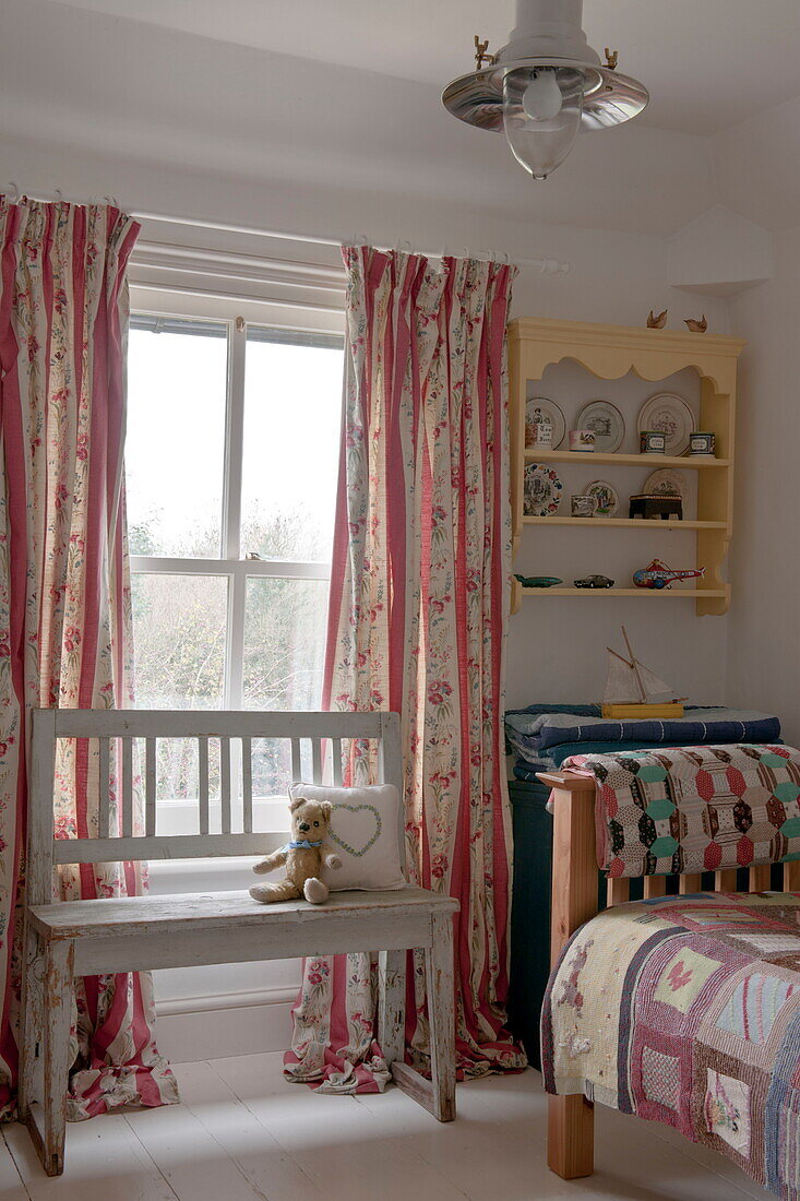 Teddy auf Sitzbank am Fenster eines Kinderzimmers in einem Haus in Ashford, Kent, England, UK