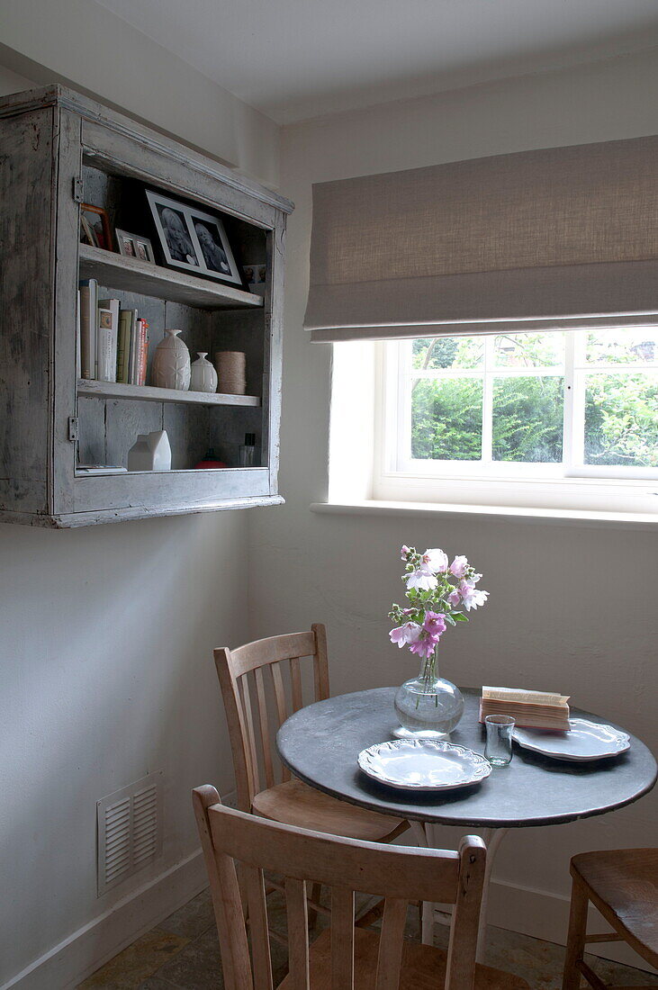 Schnittblumen auf rundem Tisch mit wandmontierten Regalen am Fenster des Hauses in Kingston, East Sussex, England, UK