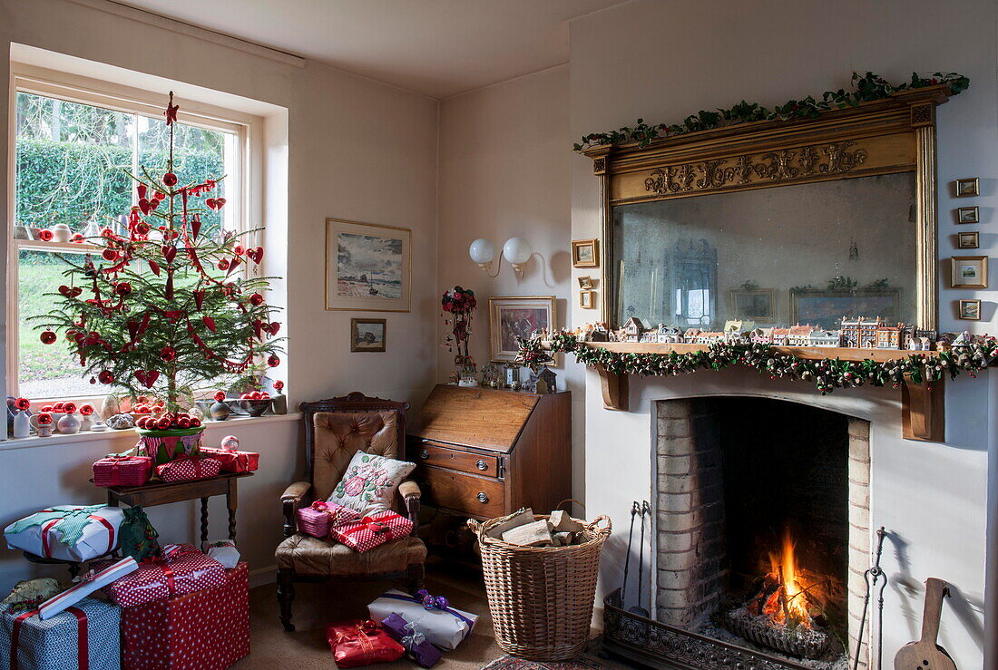 Carved wooden mirror above lit fire in Tiverton farmhouse living room with Christmas tree  Devon  UK