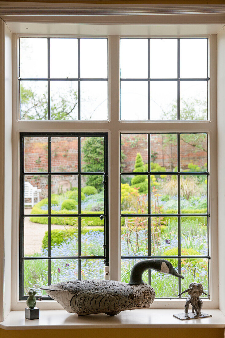 Duck ornament on leaded glass windowsill with view of Suffolk garden  England  UK