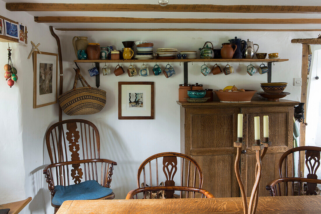 Crockery on open shelf with wooden furniture in kitchen of Devon cottage England UK
