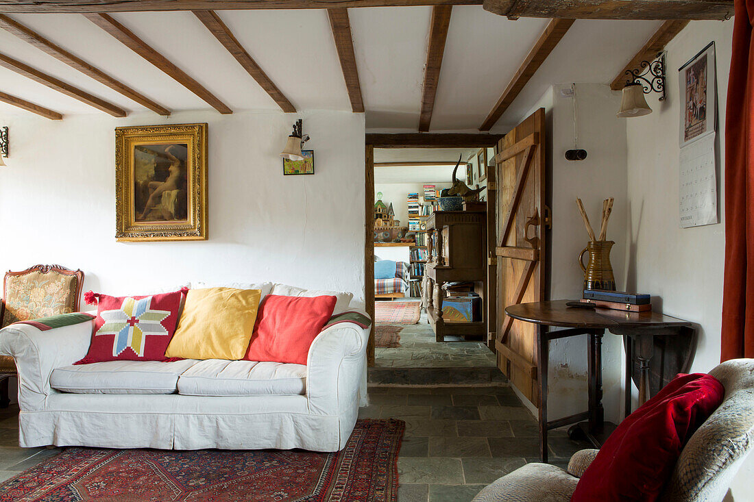 Vergoldetes gerahmtes Kunstwerk über einem weißen Sofa mit hellen Kissen in einem Cottage mit Balken in Devon, England, UK