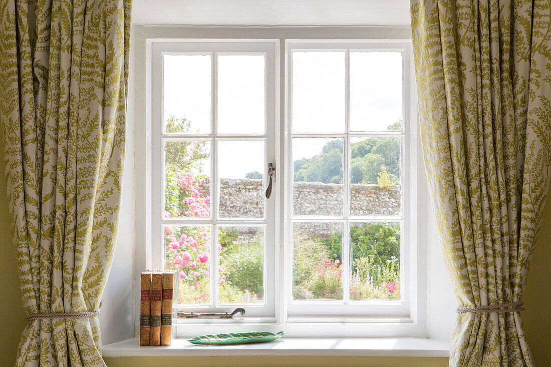 Gebundene Bücher auf der Fensterbank mit Blick auf den Garten in einem Bauernhaus in Petworth, West Sussex, Kent