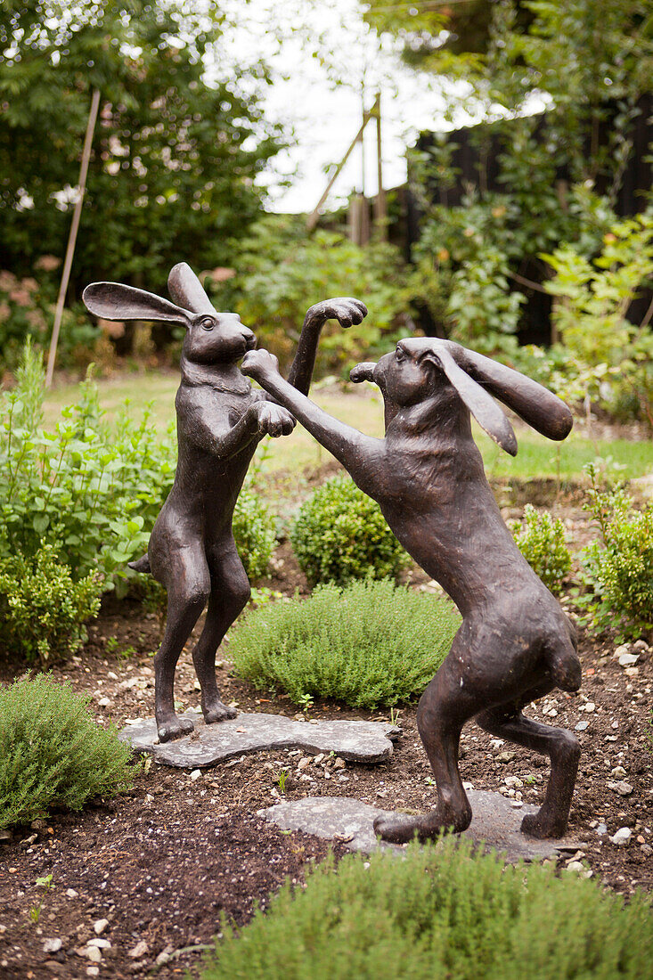 Statuen von zwei Hasen, die im Kräutergarten des Hauses in Amberley, West Sussex, England, UK, auf den Hinterbeinen miteinander kämpfen