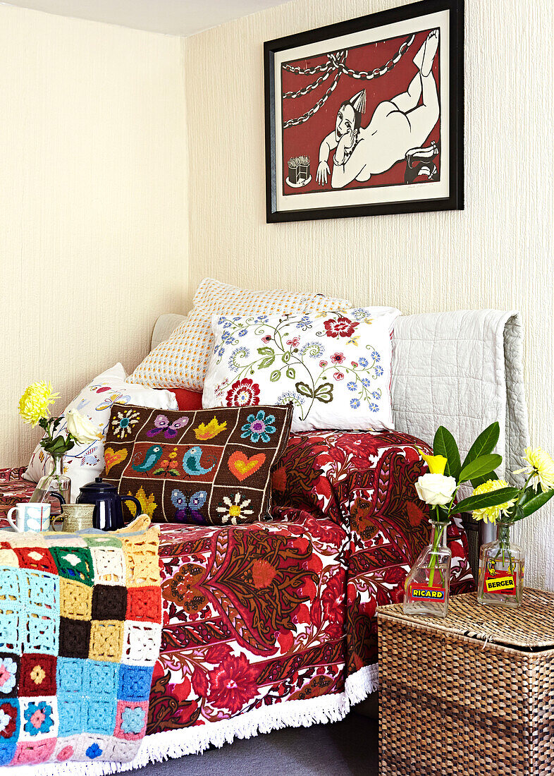 Colourful furnishings with single stem flowers on wicker laundry basket in single bedroom of Brabourne farmhouse,  Kent,  UK